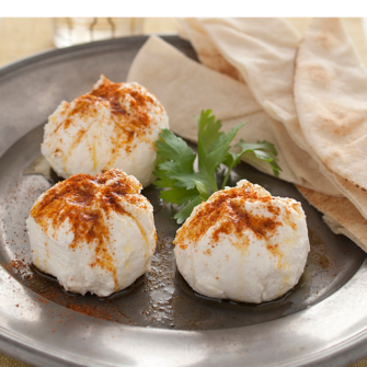 Un piatto con il formaggio di yogurt levantino chiamato labneh, tre piccole porzioni spolverizzate con paprika e servite con pane pita