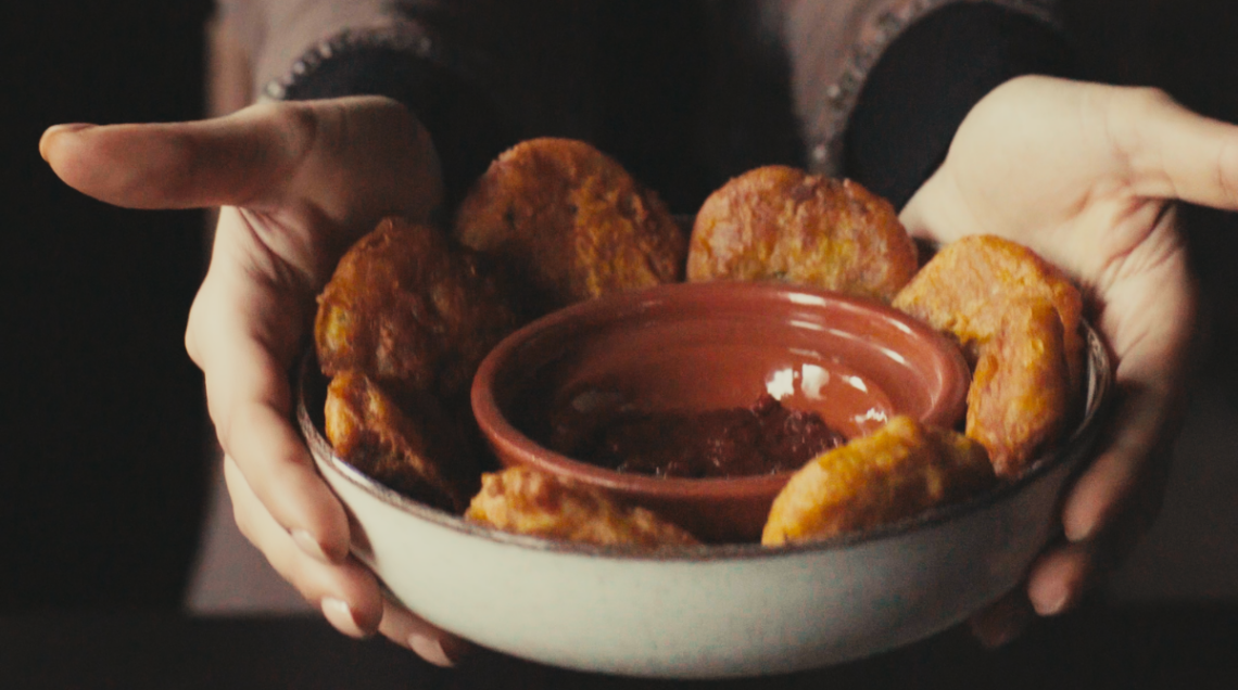 polpette di patate marocchine in una ciotola tenuta da due mani, con una scodella di salsa harissa al centro