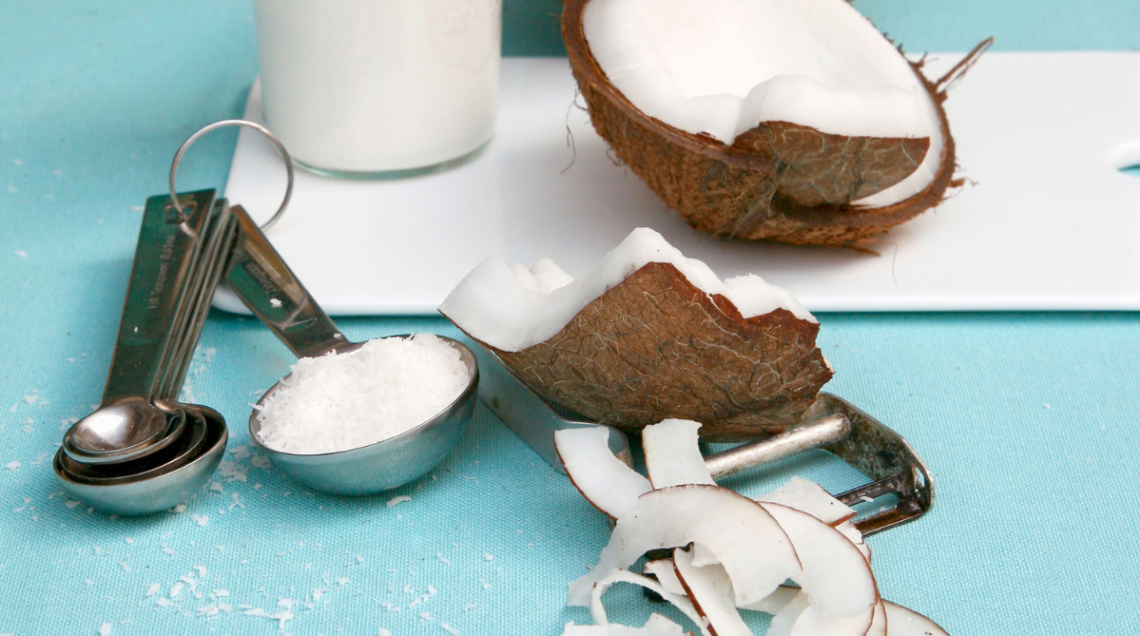 Pezzi di noci di cocco, scaglie di cocco e cocco rapé su un tavolo con sfondo azzurro