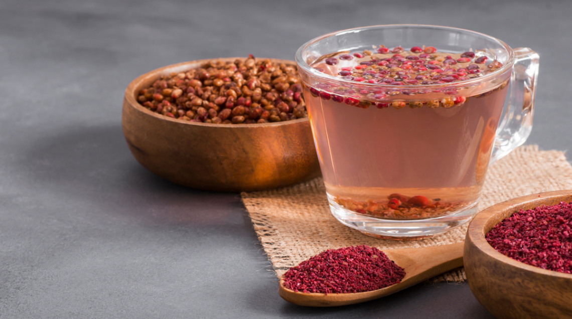 Tazza trasparente di bevanda al gusto di sommacco (Indian Lemonade), con intorno ciotoline di sommacco e un cucchiaio
