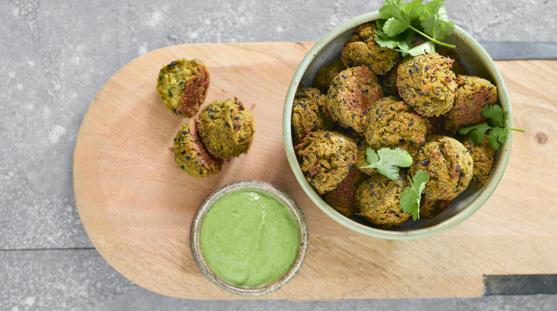 Polpette di verdure con chutney alle erbe su un vassoio di legno con piccola ciotola di salsa verde a lato