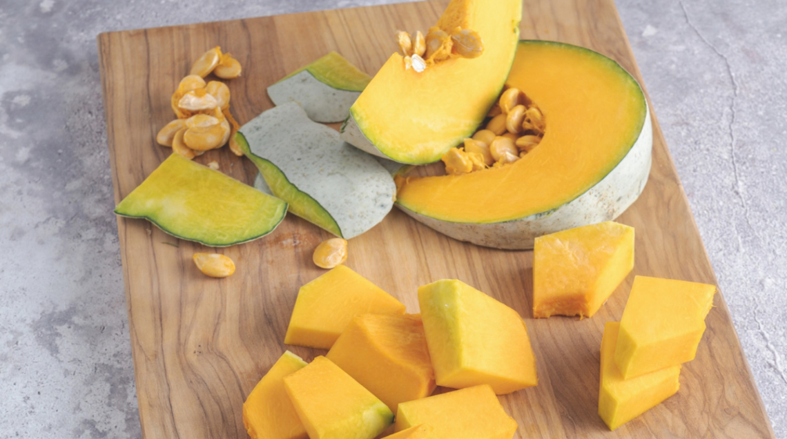 Pezzi di zucca tagliata su un tagliere di legno su un ripiano grigio