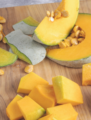 Pezzi di zucca tagliata su un tagliere di legno su un ripiano grigio
