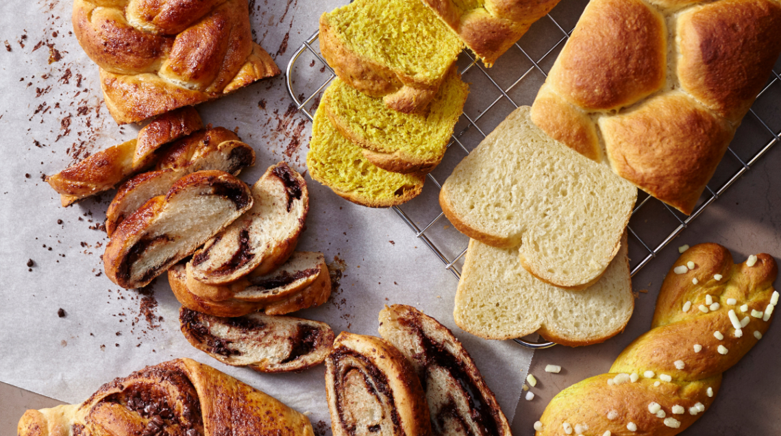 Trecce dolci e pan brioche tagliate a fette e disposte su un piano grigio