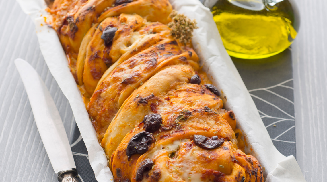 Treccia pizzata alle olive in una teglia con ampolla di olio accanto