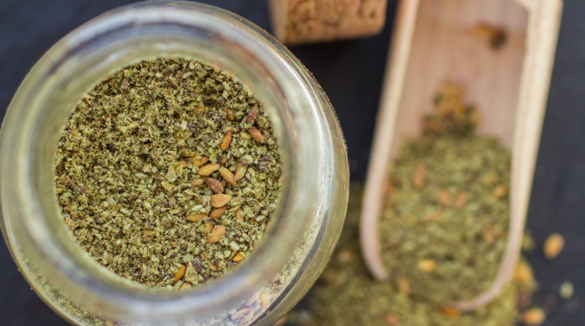 za'atar: nella foto una ciotola di vetro che contiene la miscela pronta per l'uso, con sullo sfondo, sfuocata, una piccola palettina dosatrice in legno con la miscela.