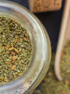 za'atar: nella foto una ciotola di vetro che contiene la miscela pronta per l'uso, con sullo sfondo, sfuocata, una piccola palettina dosatrice in legno con la miscela.