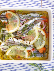acciughe marinate in un piatto quadrato con fette di limone. il piatto è appoggiato su un tavolo piastrellato, c'è un limone tagliato a metà accanto