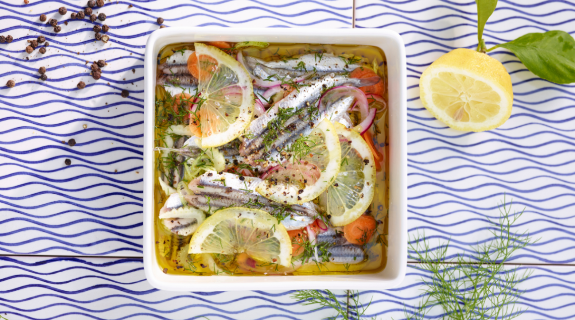 acciughe marinate con fette di limone in un piatto quadrato adagiato su una superficie ricoperta di piastrelle blu e bianche