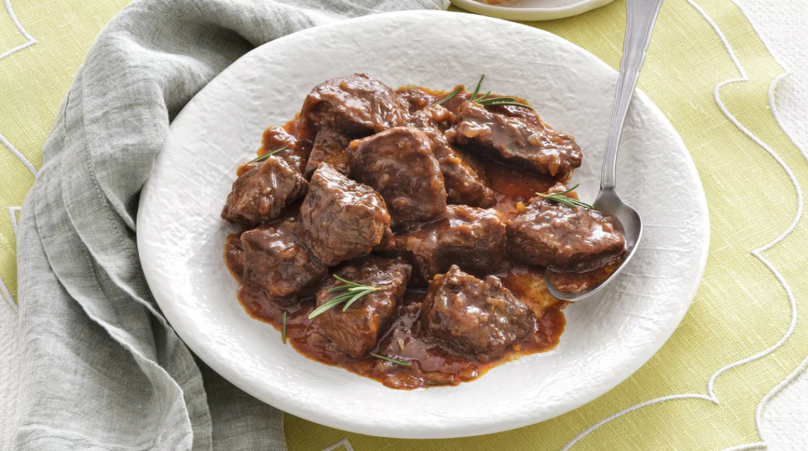 un piatto bianco con un canovaccio grigio sotto contenente cinghiale in umido
