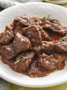 un piatto bianco con un canovaccio grigio sotto contenente cinghiale in umido