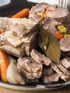 bollito di carne in una teglia nera rotonda con sedano e carote, su un tagliere di legno