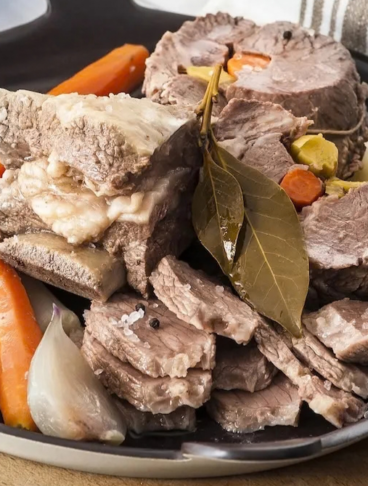bollito di carne in una teglia nera rotonda con sedano e carote, su un tagliere di legno