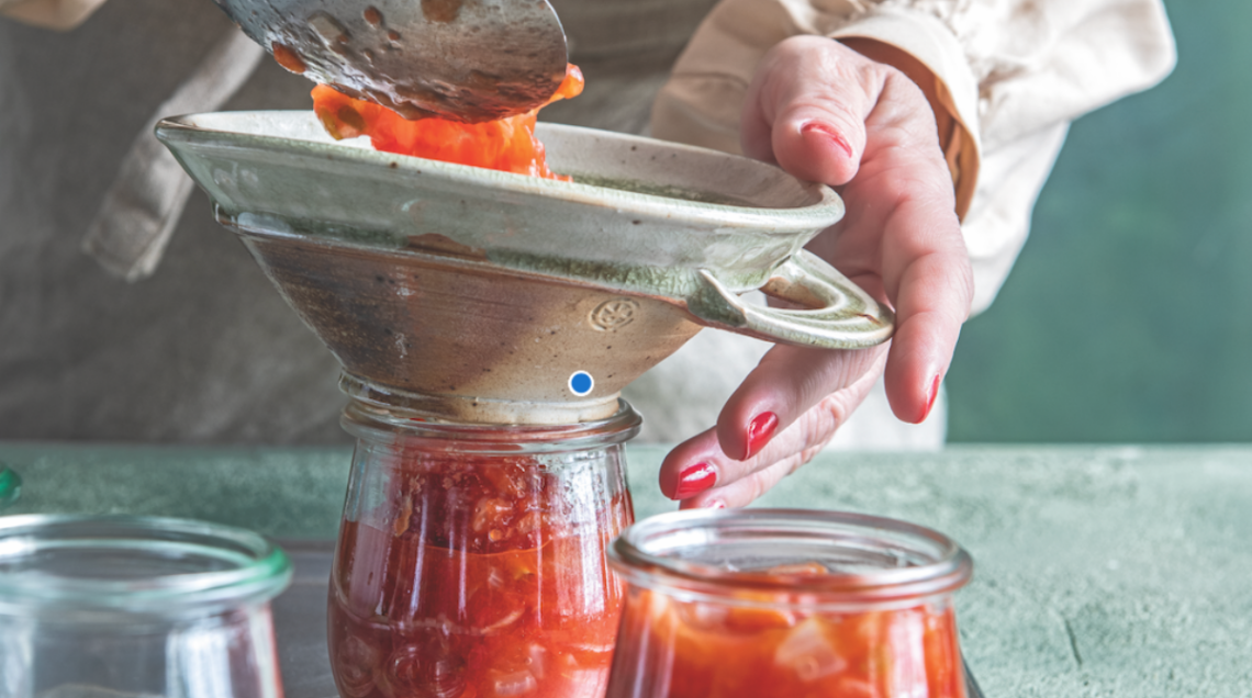 due mani versano del pomodoro in un imbuto posto sopra un vasettino di vetro