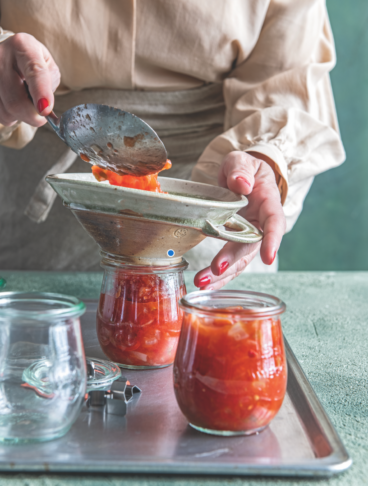 due mani versano del pomodoro in un imbuto posto sopra un vasettino di vetro