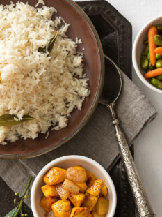 Piatto di riso e ciotole con condimenti di patate, carote e fave, frutta secca