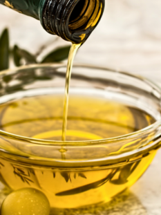 da una bottiglia viene versato dell'olio all'interno di una ciotolina di vetro, affianco alla quale vi sono delle olive