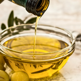 da una bottiglia viene versato dell'olio all'interno di una ciotolina di vetro, affianco alla quale vi sono delle olive