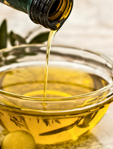 da una bottiglia viene versato dell'olio all'interno di una ciotolina di vetro, affianco alla quale vi sono delle olive
