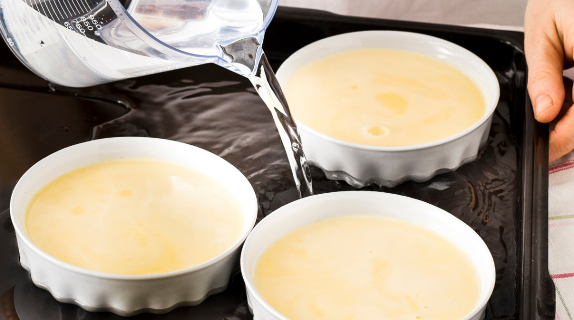 tre ciotole bianche ripiene di crème brûlée sono in una teglia da forno nera con acqua