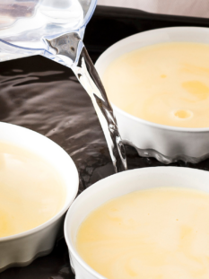 tre ciotole bianche ripiene di crème brûlée sono in una teglia da forno nera con acqua