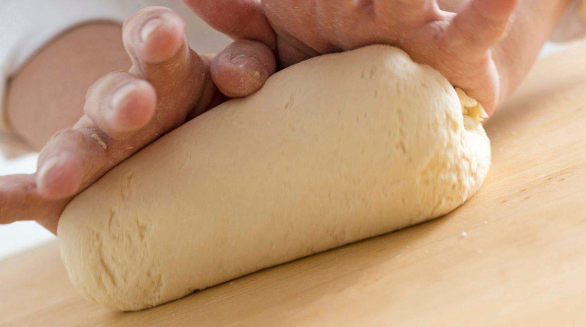 due mani impastano la pasta violada su un tagliere di legno