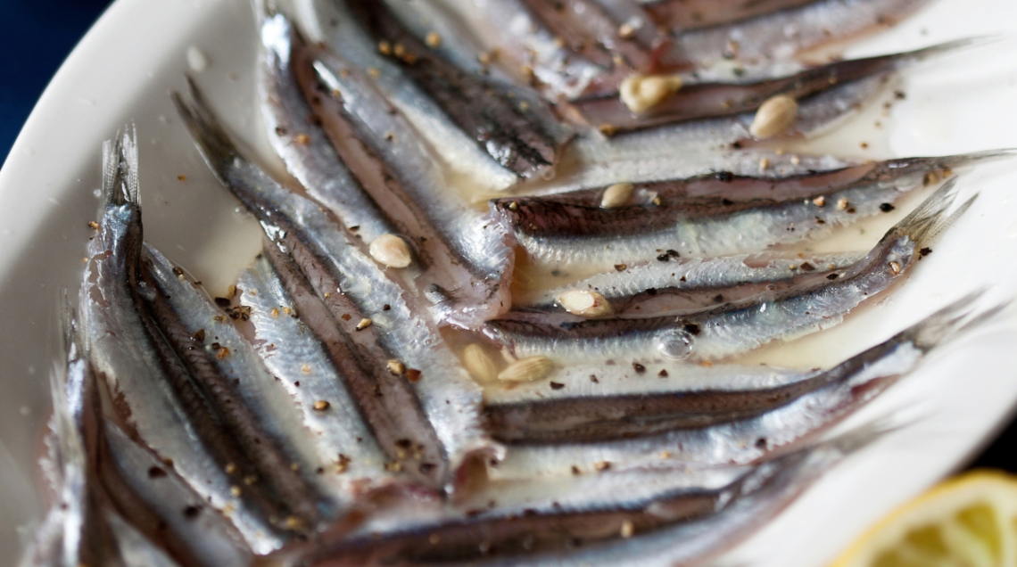 su un piatto bianco ovale sono disposte delle acciughe condite con olio, aglio, limone e peperoncino