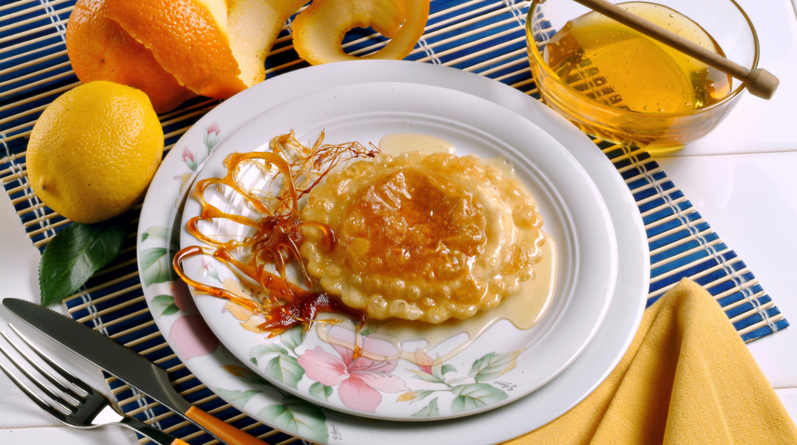 seadas impiattata su doppio piatto piano e circondata da un limone, buccia di mela, miele, posate e un tovagliolo giallo ocra