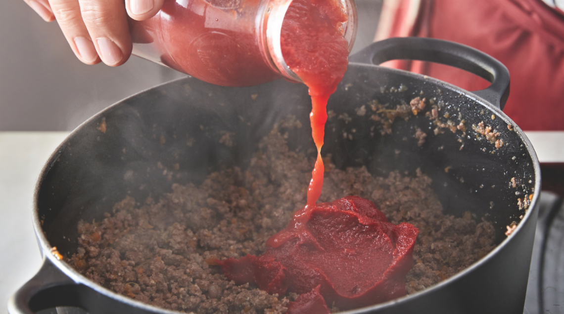 pentola di ragu sul fuoco mentre viene versato del sugo di pomodoro