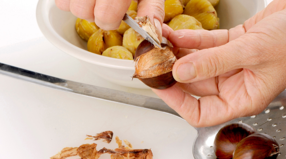 una persona sta sbucciando le castagne con l'apposito utensile