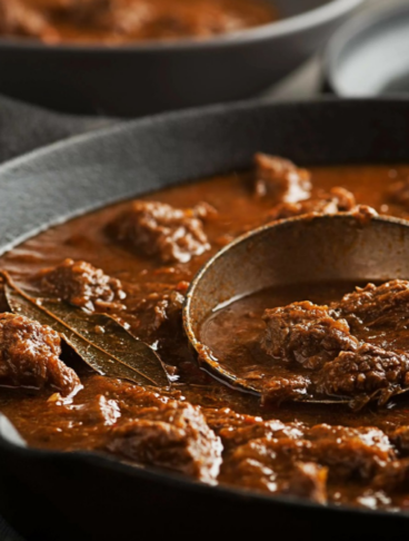 Spezzatino ungherese, gulash, caldo in una padella di ghisa, con un mestolo per servire