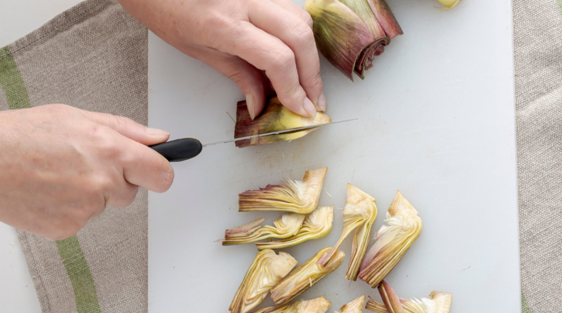Mani che tagliano dei carciofi su un tagliere
