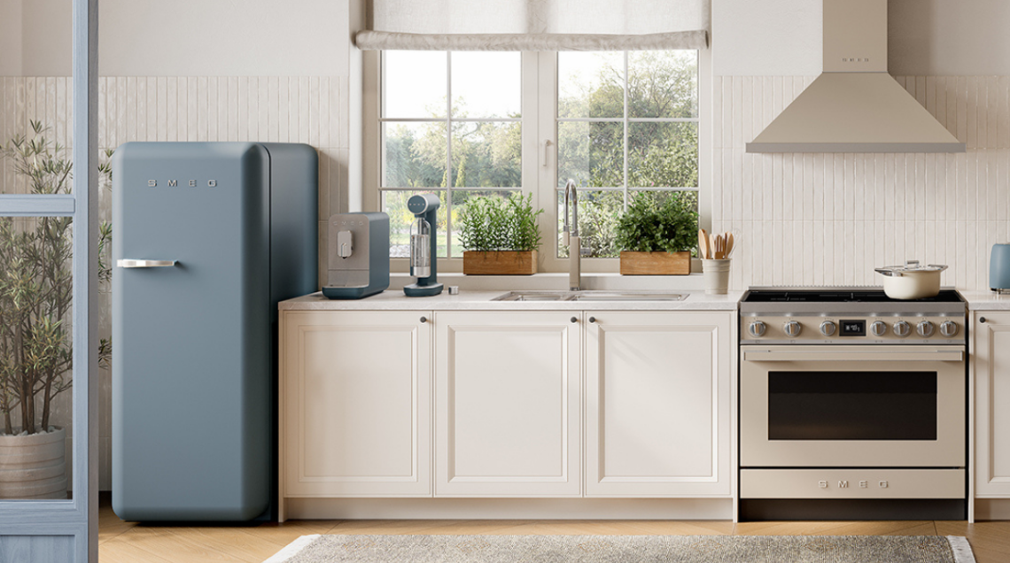 Un frigorifero Smeg azzurro dal design rétro in una cucina luminosa con mobili bianchi, piano di lavoro in marmo e grandi finestre sul giardino