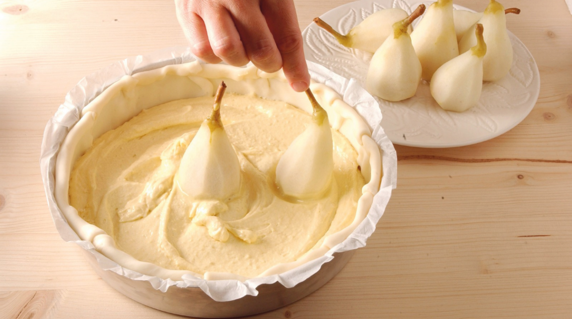 mano che aggiunge pere alla base di una torta ancora cruda