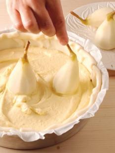 mano che aggiunge pere alla base di una torta ancora cruda