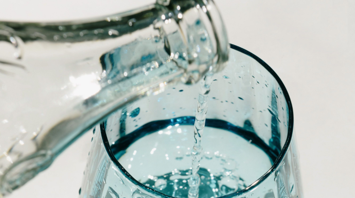 versando acqua da un bottiglia di vetro in un bicchiere di vetro azzurro