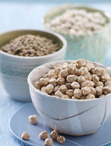 tre ciotoline su sfondo di legno azzurro riempite con legumi (ceci, lenticchie e fagioli bianchi)