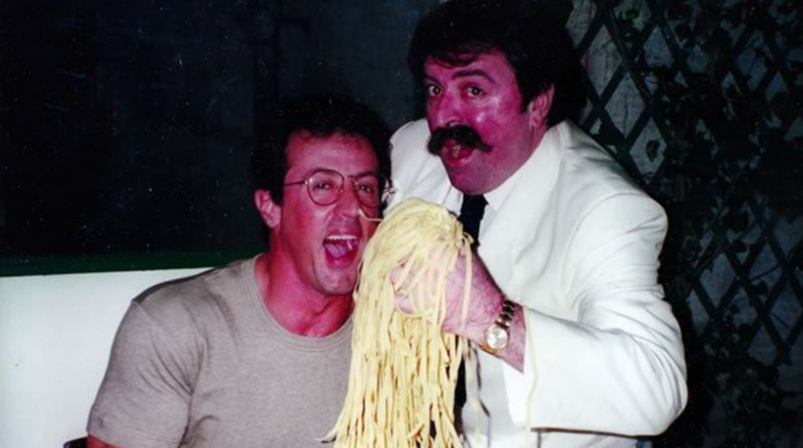 Una vecchia foto del Ristorante Vecchio Alfredo dove due uomini stanno per addentare una manciata di fettuccine