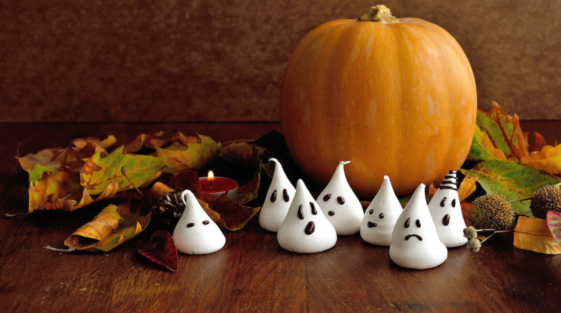 zucca arancione con foglie secche e meringhette a forma di fantasmini disposte su un tavolo di legno