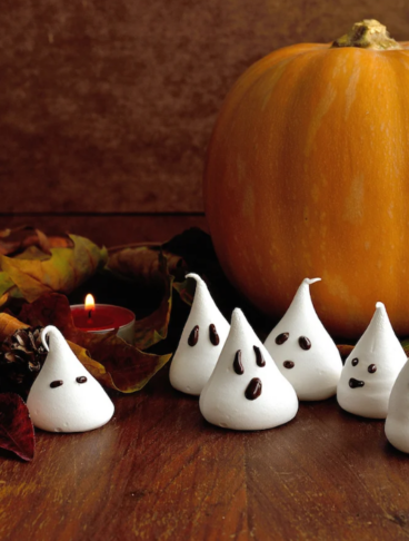 zucca arancione con foglie secche e meringhette a forma di fantasmini disposte su un tavolo di legno