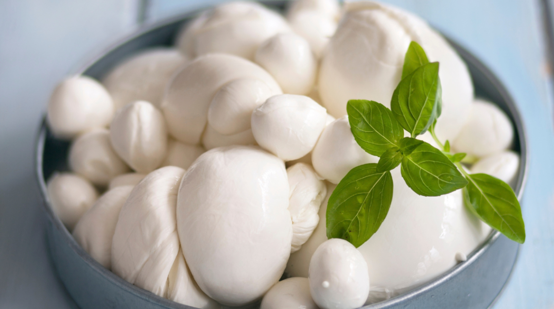 mozzarelle di diverse forme all'interno di una ciotola azzurra, decorate con qualche foglia di basilico