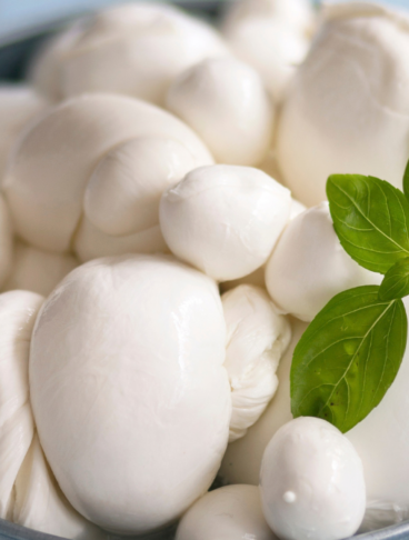 mozzarelle di diverse forme all'interno di una ciotola azzurra, decorate con qualche foglia di basilico