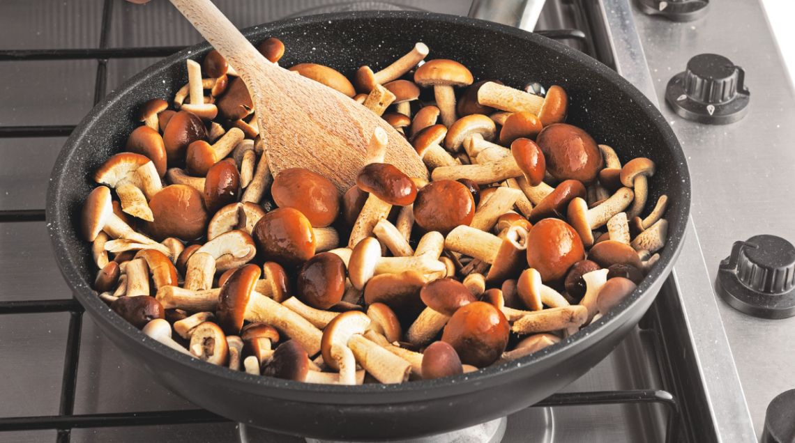 una pentola antiaderente con funghi in cottura e un cucchiaio di legno