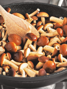 una pentola antiaderente con funghi in cottura e un cucchiaio di legno