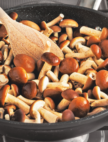 una pentola antiaderente con funghi in cottura e un cucchiaio di legno