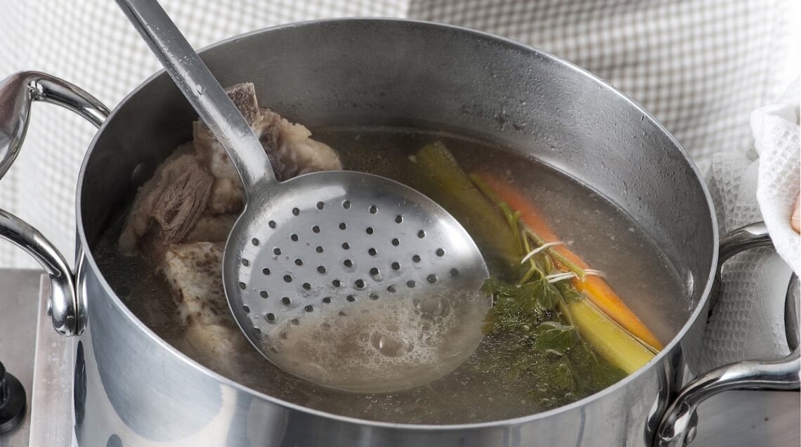 brodo di carne schiumato con un mestolo forato