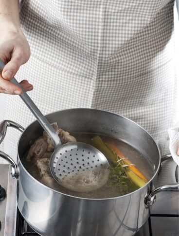 brodo di carne schiumato con un mestolo forato